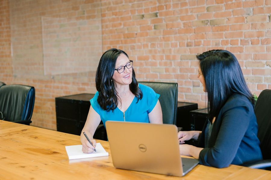 Two colleagues talking at a table with a laptop